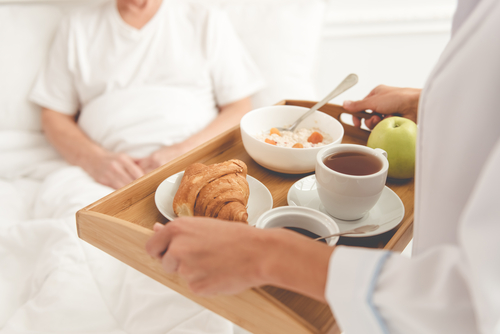 A Medical worker bringing a male patient breakfast on a tray in bed.