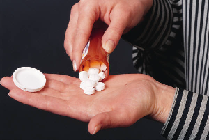 Female has a bottle of pills pouring out onto her hand.